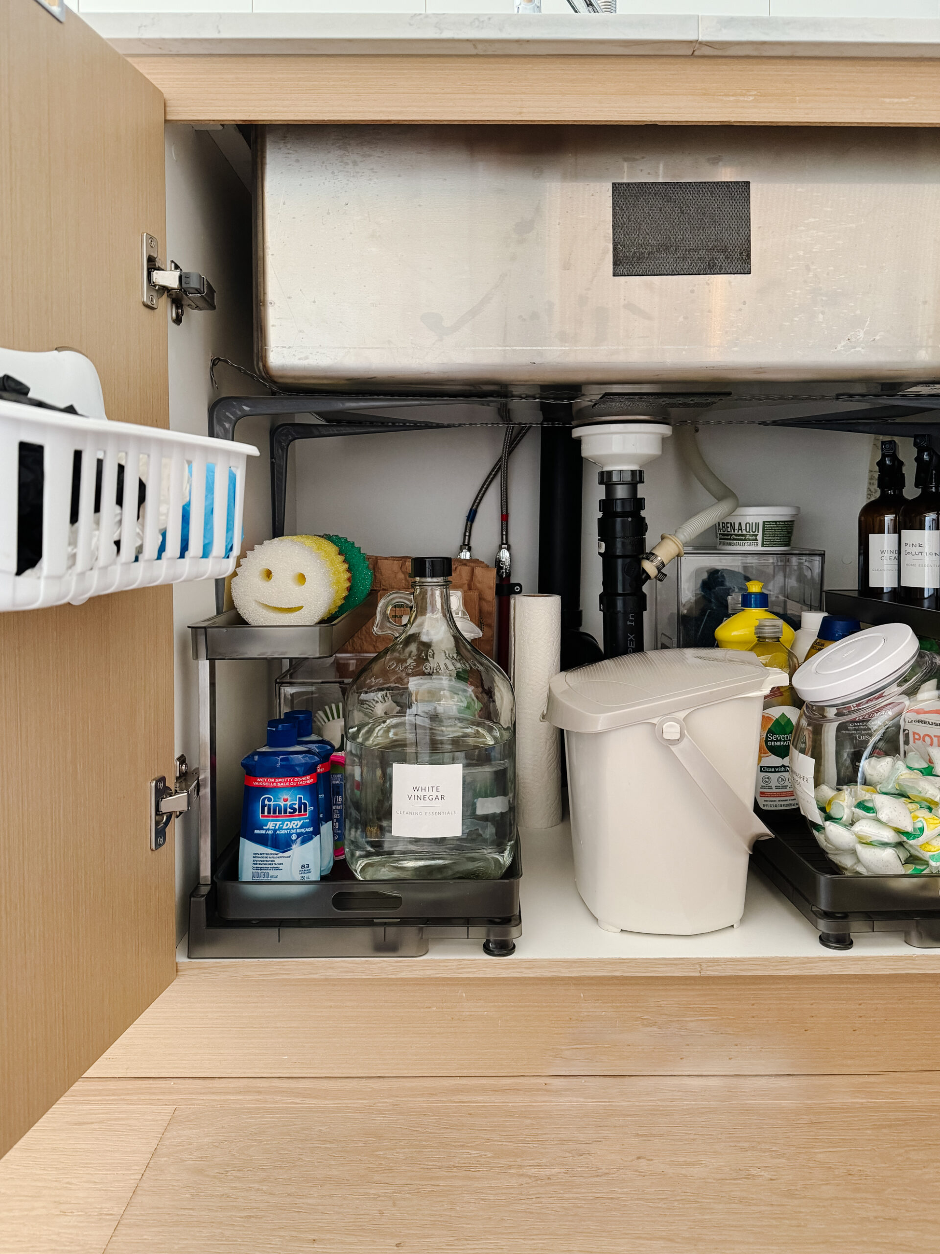 under the kitchen sink organization with a pull out drawer, glass container for vinegar, scrub daddys and more cleaning supplies