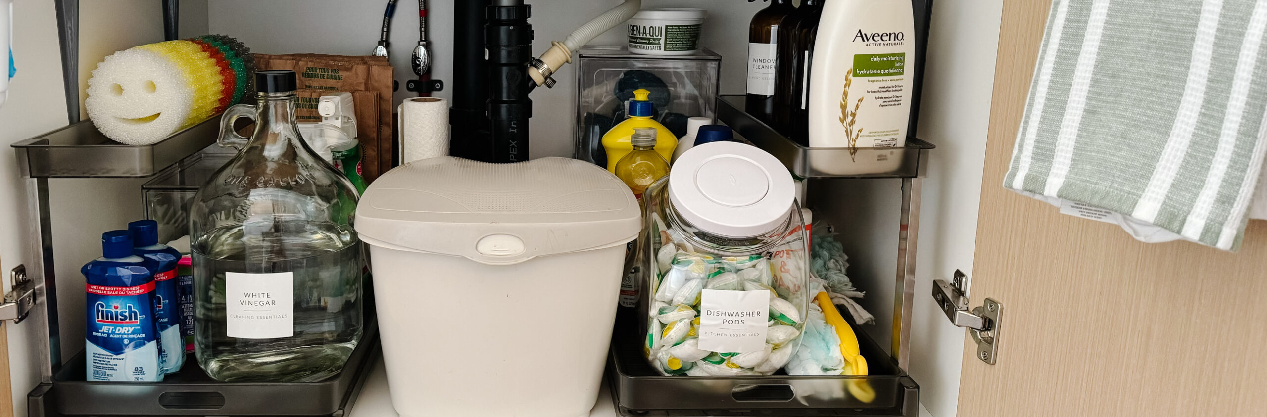 under the kitchen sink organization with a pull out drawer, glass container for vinegar, scrub daddys and more cleaning supplies