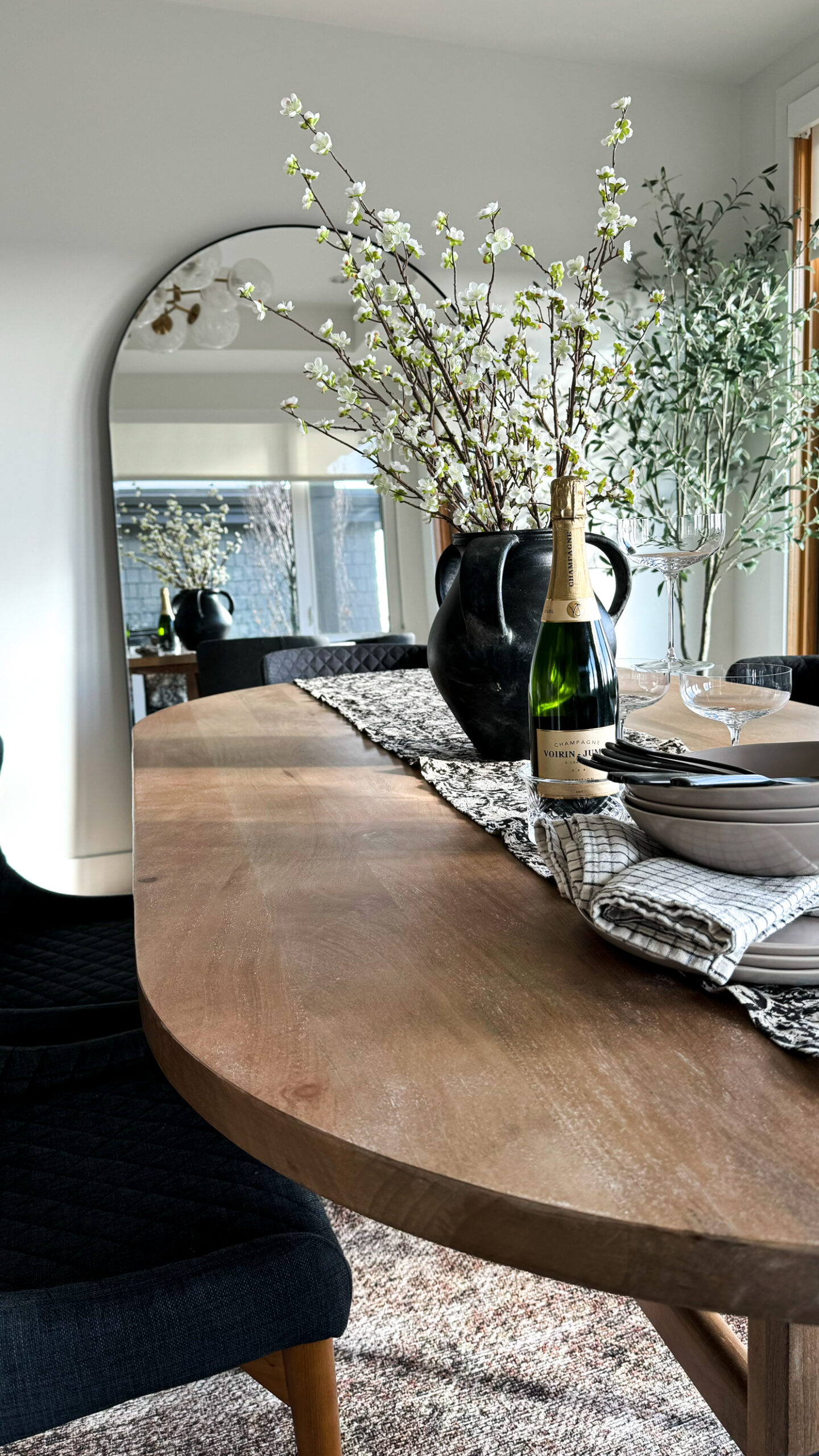 Dining room shot of the dining table with plates bowls champagne flutes florals and a runner on it. Dining room shot of the dining table with plates bowls champagne flutes florals and a runner on it. Oversized mirror in the background and olive treeDining room shot of the dining table with plates bowls champagne flutes florals and a runner on it. Dining room shot of the dining table with plates bowls champagne flutes florals and a runner on it. Oversized mirror in the background and olive tree