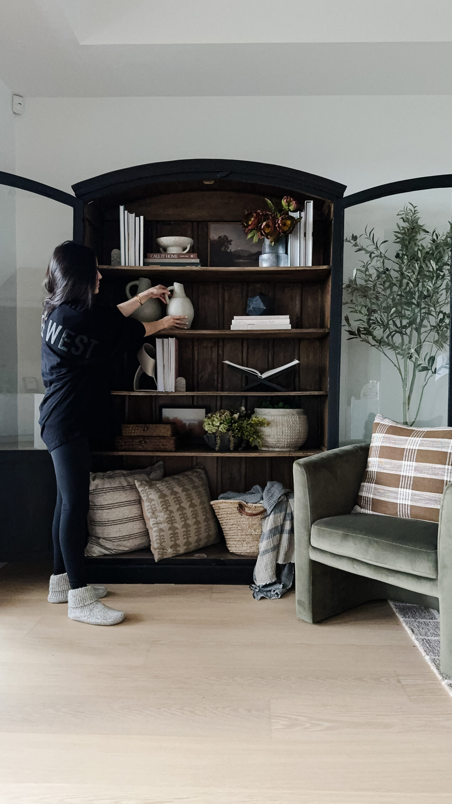 signed samantha styling shelves in her black arched cabinet. the shelves have books, plants, vases, and other decorative objects on it.