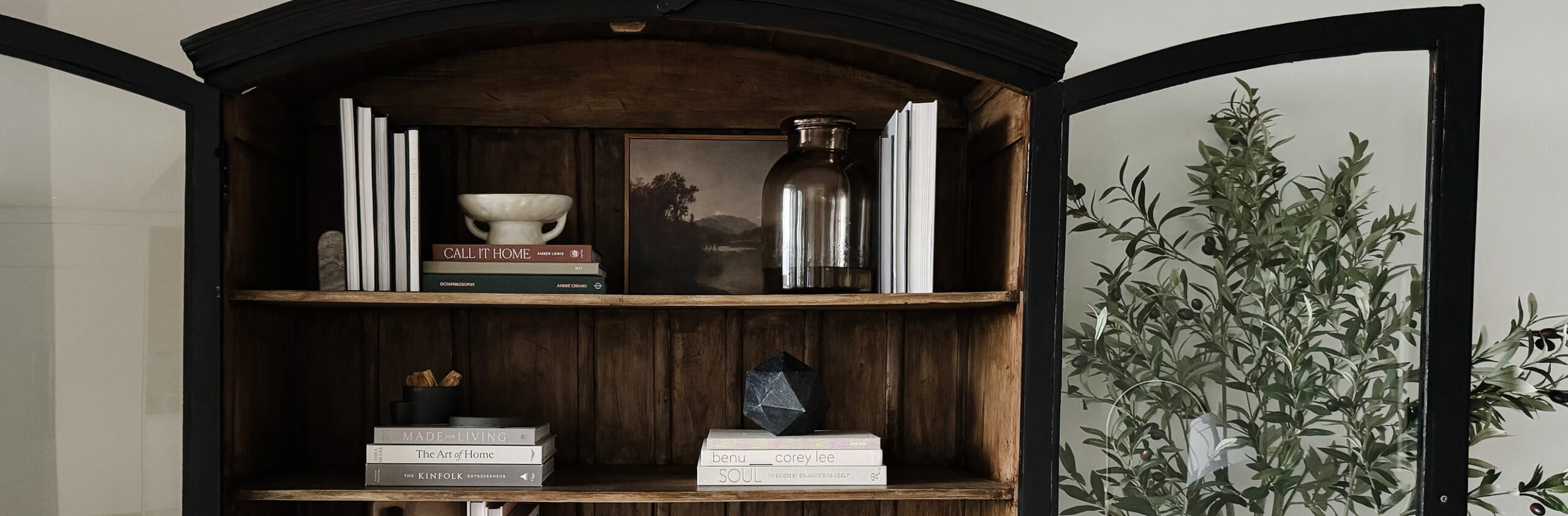 Styling Shelves - a black bookshelf cabinet that is arched with wood interior having been styled with vases, pots, books, etc. is on display